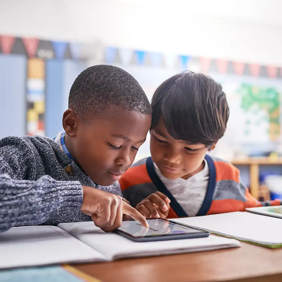 two little boys in school using ipad for homework, heads close together - lice can spread fast and easily - St. Charles, MO