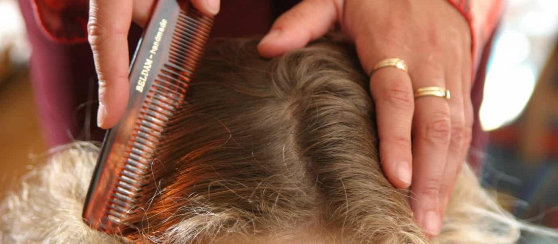 Mother gently combing through little girl's hair checking for head lice