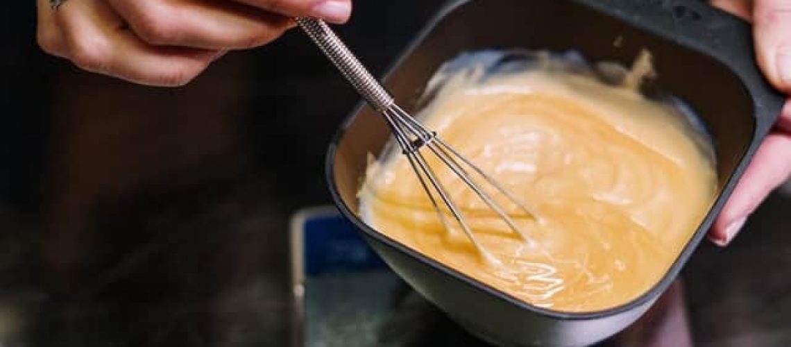 person mixing hair bleach in black bowl with wire wisk