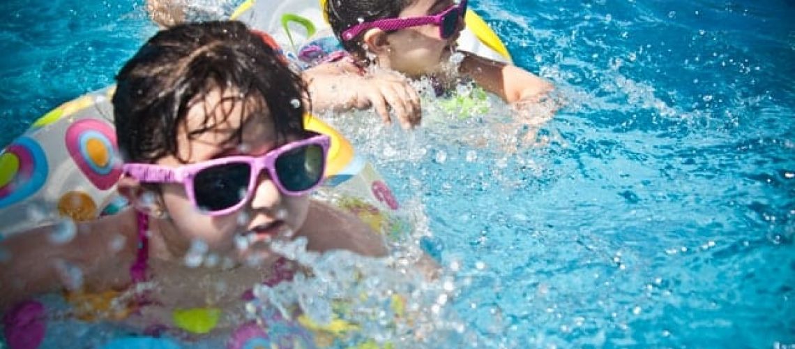 two children swimming in a pool with floaties and goggles on a sunny summer day